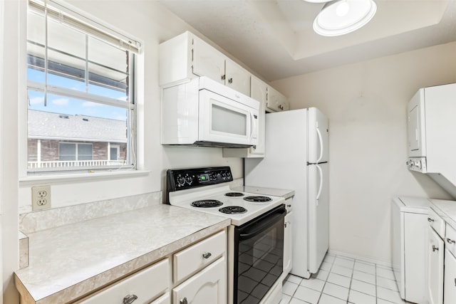 kitchen featuring electric stove, stacked washer and dryer, and white cabinetry