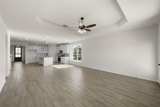 unfurnished living room with a raised ceiling, ceiling fan, sink, and wood-type flooring