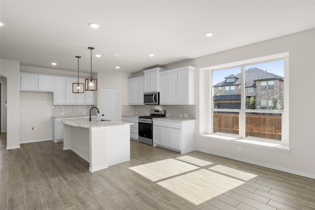 kitchen with white cabinetry, hanging light fixtures, light hardwood / wood-style flooring, an island with sink, and appliances with stainless steel finishes