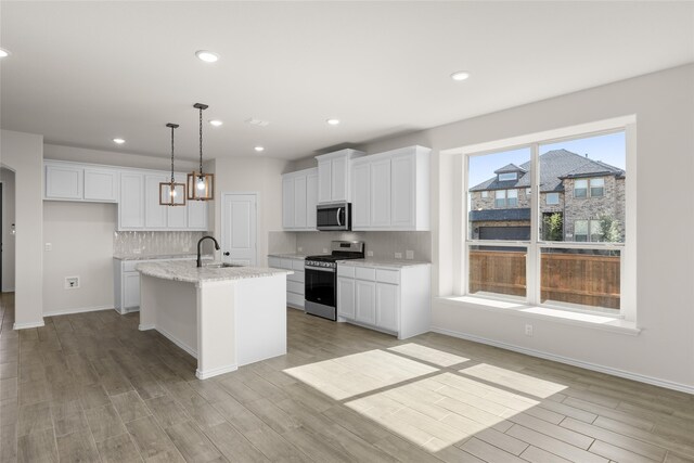 kitchen featuring sink, decorative light fixtures, an island with sink, stainless steel appliances, and white cabinets