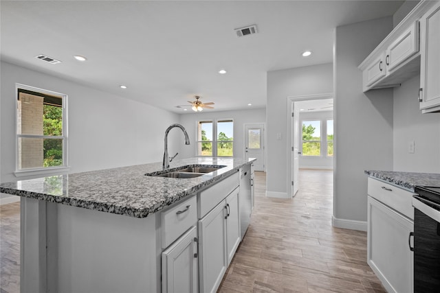 kitchen featuring light stone countertops, a kitchen island with sink, sink, and ceiling fan