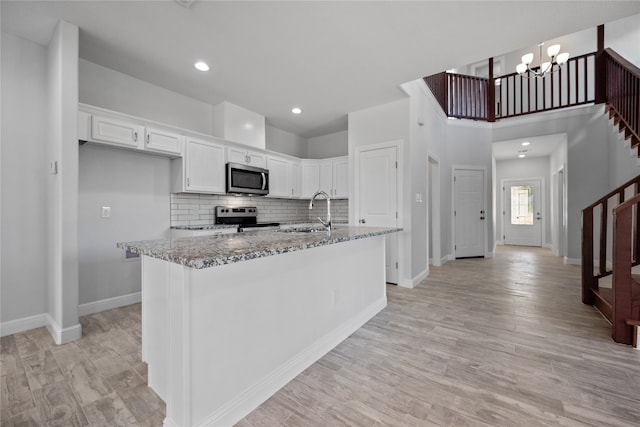 kitchen featuring a notable chandelier, light stone counters, stainless steel appliances, and white cabinets