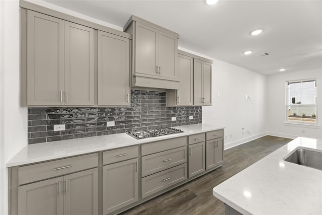 kitchen with gray cabinetry, light stone countertops, stainless steel gas cooktop, dark hardwood / wood-style floors, and decorative backsplash