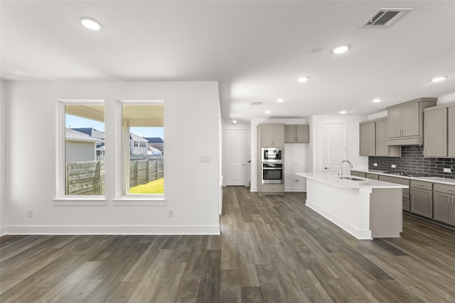 kitchen with a center island with sink, sink, appliances with stainless steel finishes, and dark wood-type flooring