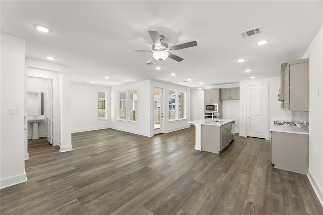 kitchen featuring gray cabinetry, ceiling fan, built in microwave, sink, and an island with sink