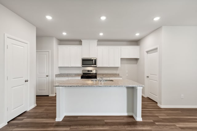 kitchen featuring dark stone countertops, white cabinets, an island with sink, and sink