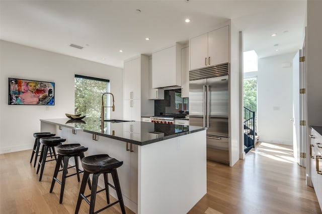 kitchen with white cabinetry, tasteful backsplash, built in fridge, light hardwood / wood-style flooring, and sink