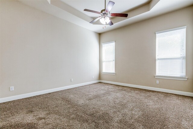 carpeted spare room featuring a tray ceiling and ceiling fan