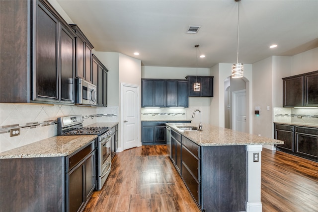 kitchen featuring an island with sink, hanging light fixtures, sink, dark wood-type flooring, and appliances with stainless steel finishes