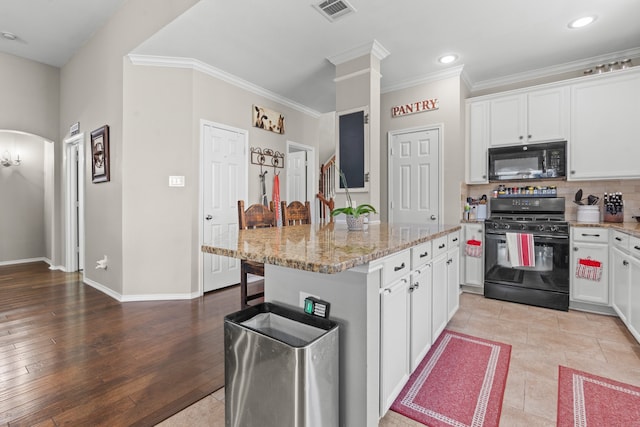 kitchen with white cabinets, light wood-type flooring, a center island, and black appliances