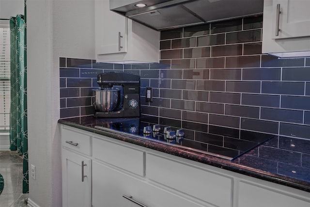 kitchen with decorative backsplash, white cabinets, black stovetop, range hood, and dark stone counters