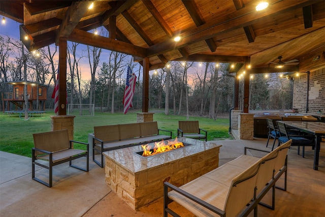 patio terrace at dusk featuring a fire pit, a trampoline, and a yard