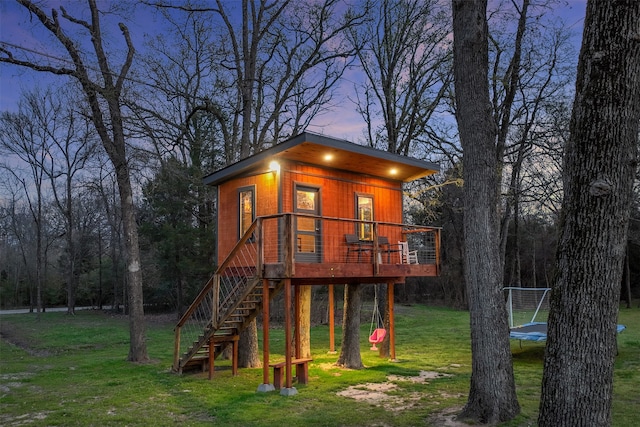 back house at dusk with a trampoline, a deck, and a lawn