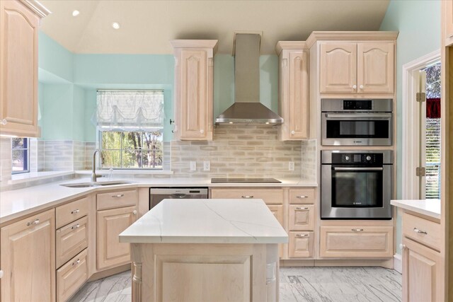 kitchen with light brown cabinetry, lofted ceiling, wall chimney exhaust hood, and sink