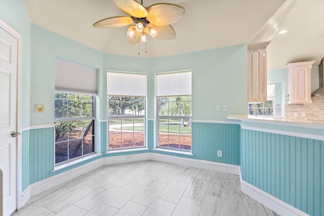 unfurnished dining area with wainscoting, a wealth of natural light, a ceiling fan, and marble finish floor