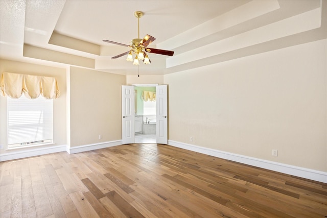empty room featuring a raised ceiling, ceiling fan, wood-type flooring, and baseboards