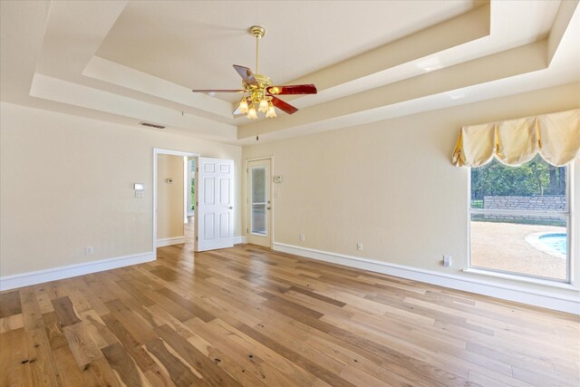 spare room with ceiling fan, a tray ceiling, and light hardwood / wood-style floors