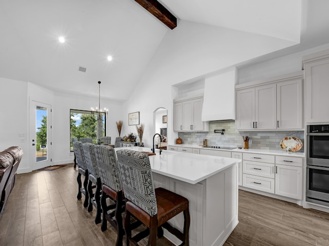 kitchen featuring black electric stovetop, beamed ceiling, a kitchen island with sink, dark wood-type flooring, and an inviting chandelier