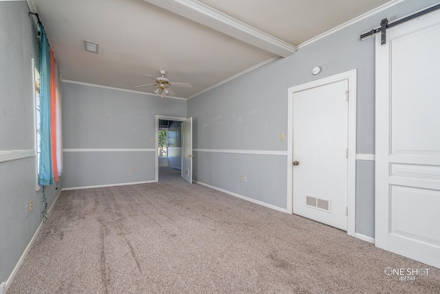 carpeted spare room featuring ceiling fan, crown molding, and a barn door