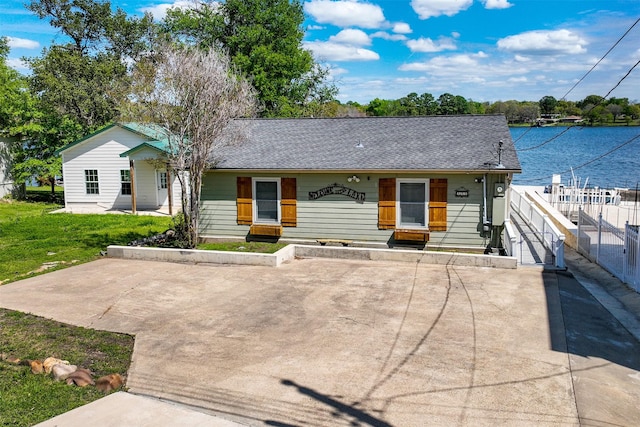 single story home with a front lawn, a water view, fence, and roof with shingles