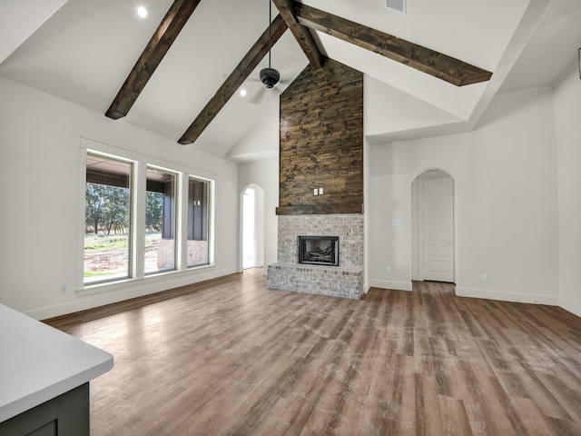 unfurnished living room with a large fireplace, high vaulted ceiling, hardwood / wood-style floors, and beamed ceiling