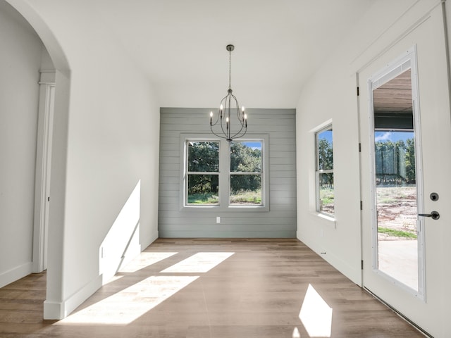 unfurnished dining area with an inviting chandelier, wooden walls, and light hardwood / wood-style flooring