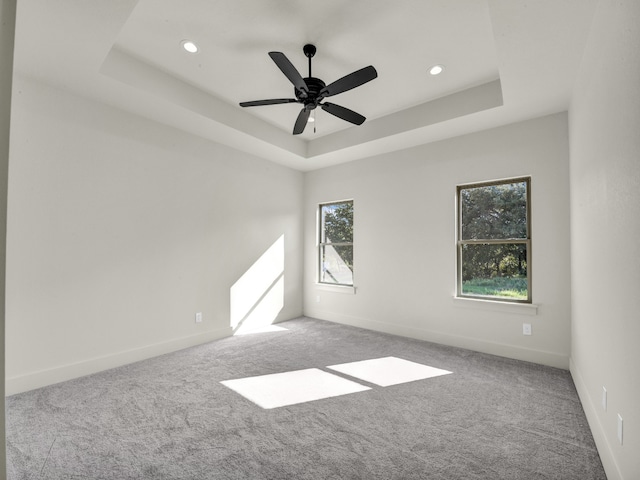 empty room with a raised ceiling, carpet floors, and ceiling fan