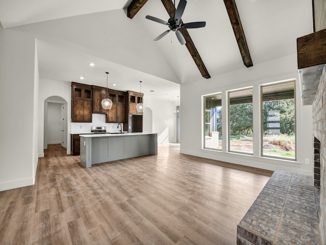 unfurnished living room featuring ceiling fan, beam ceiling, light hardwood / wood-style flooring, a fireplace, and high vaulted ceiling