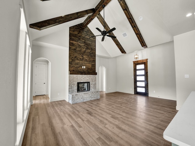 unfurnished living room featuring hardwood / wood-style flooring, high vaulted ceiling, a brick fireplace, and beamed ceiling