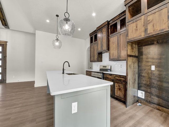 kitchen with an island with sink, sink, light hardwood / wood-style floors, decorative light fixtures, and stainless steel electric range