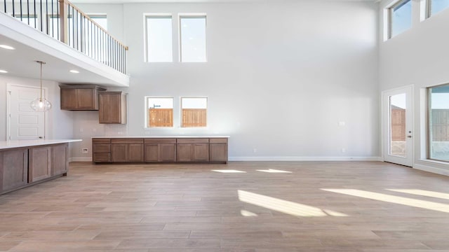 unfurnished living room with light wood-style flooring, a high ceiling, and baseboards