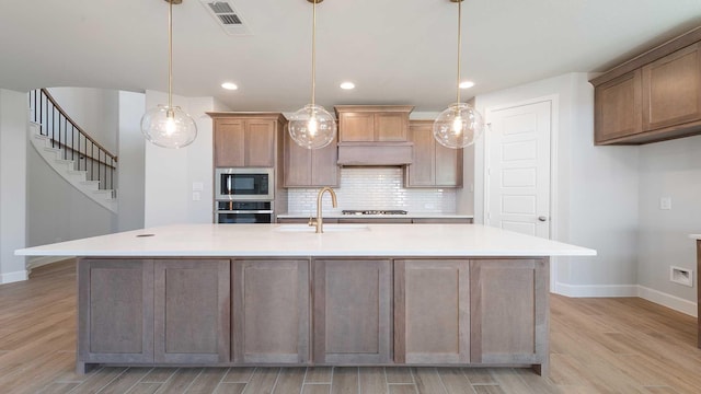 kitchen featuring light wood finished floors, appliances with stainless steel finishes, backsplash, and a sink