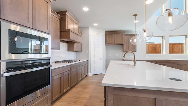 kitchen featuring pendant lighting, decorative backsplash, appliances with stainless steel finishes, a sink, and light wood-type flooring