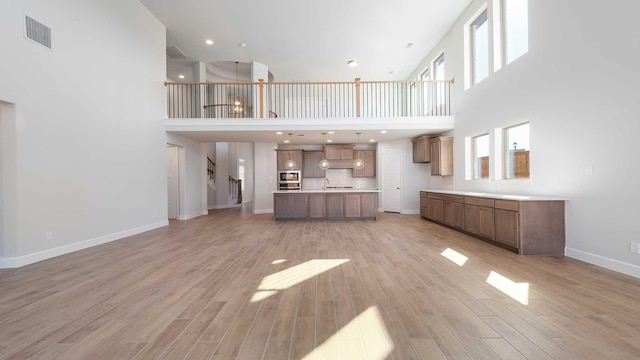 unfurnished living room with light wood-type flooring, visible vents, stairway, and baseboards