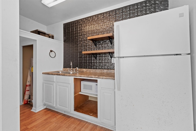 kitchen featuring white appliances, white cabinets, sink, decorative backsplash, and light wood-type flooring