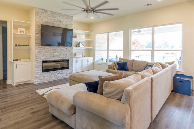 living room featuring ceiling fan, a stone fireplace, built in shelves, and wood-type flooring