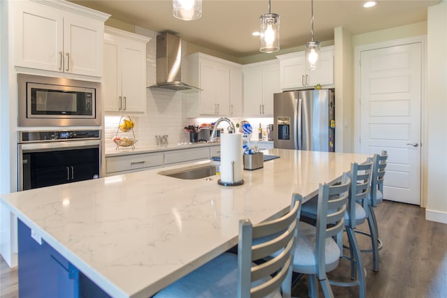 kitchen with a kitchen island with sink, wall chimney range hood, stainless steel appliances, and white cabinets