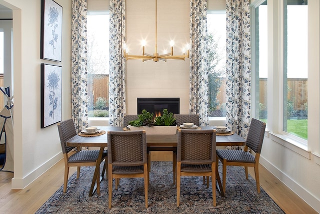 dining room with a notable chandelier, hardwood / wood-style flooring, a fireplace, and a healthy amount of sunlight