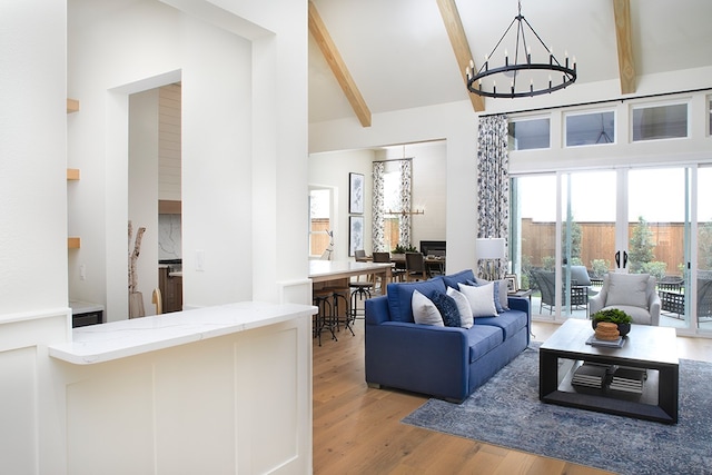 living room with an inviting chandelier, light hardwood / wood-style flooring, beam ceiling, and high vaulted ceiling