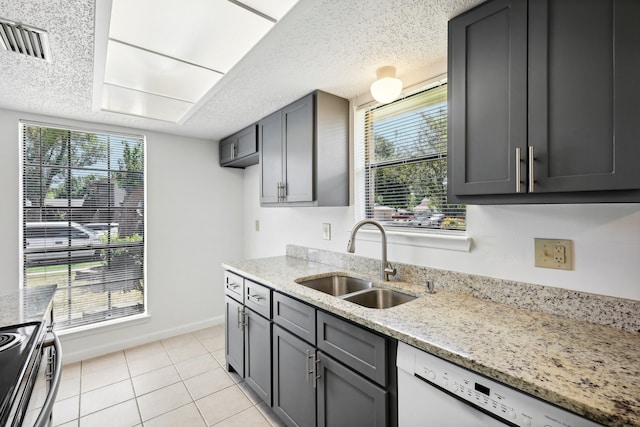 kitchen with dishwasher, sink, light tile patterned floors, and light stone counters