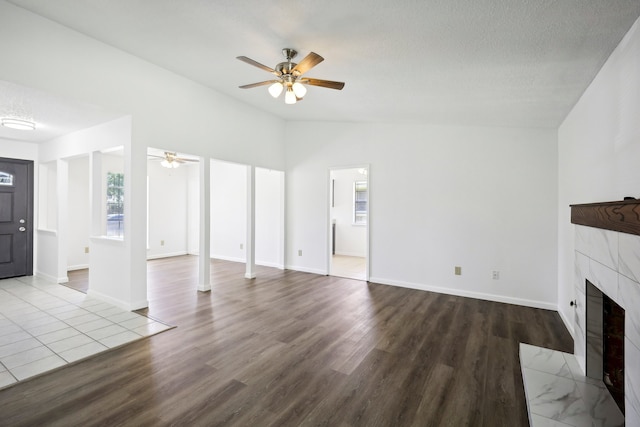 unfurnished living room with ceiling fan, vaulted ceiling, wood-type flooring, and a tile fireplace