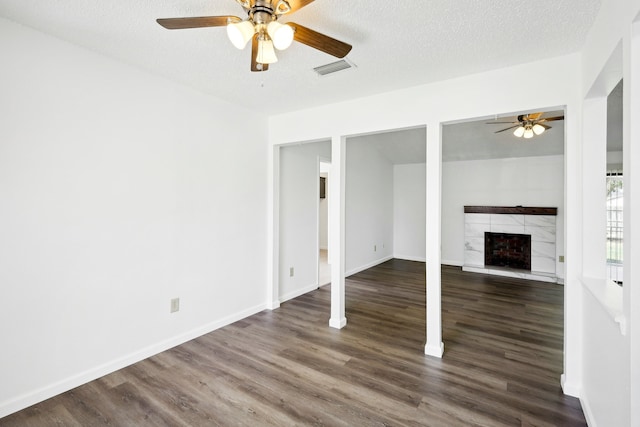 unfurnished living room with ceiling fan, a tile fireplace, dark wood-type flooring, and a textured ceiling