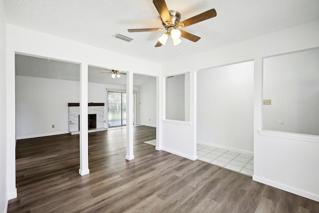 empty room with a textured ceiling, a tiled fireplace, ceiling fan, and hardwood / wood-style flooring