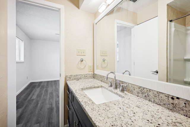 bathroom with a textured ceiling, hardwood / wood-style flooring, vanity, and a shower