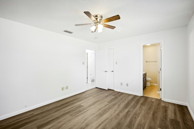 unfurnished bedroom with a textured ceiling, hardwood / wood-style floors, ceiling fan, and ensuite bathroom