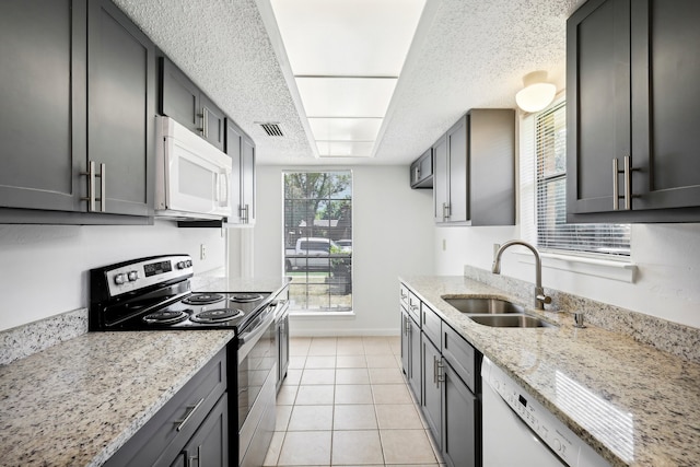 kitchen featuring light tile patterned floors, sink, white appliances, a textured ceiling, and light stone countertops