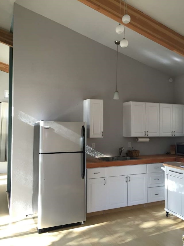 kitchen with pendant lighting, beam ceiling, white cabinetry, high vaulted ceiling, and stainless steel fridge