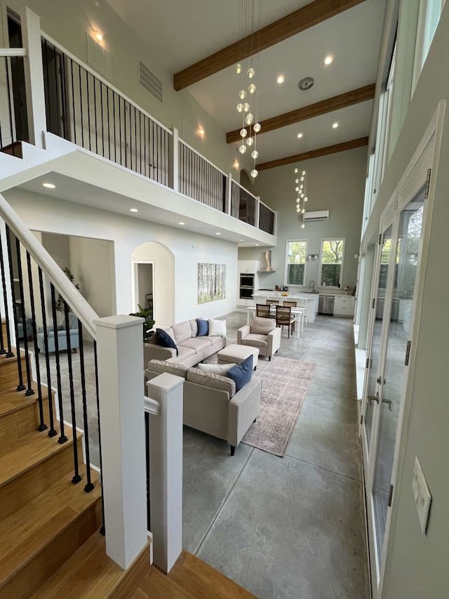 living room with wood-type flooring, a high ceiling, beam ceiling, and an inviting chandelier