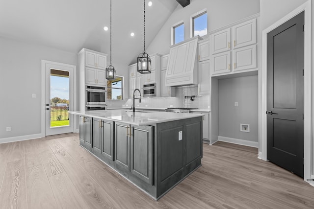 kitchen with a kitchen island with sink, sink, pendant lighting, white cabinetry, and lofted ceiling