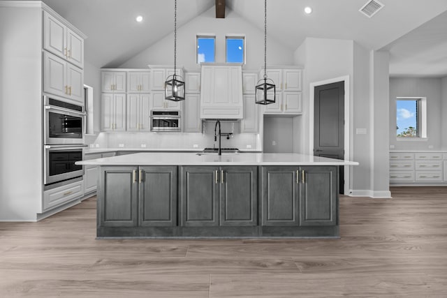 kitchen featuring backsplash, sink, decorative light fixtures, a center island with sink, and light hardwood / wood-style flooring